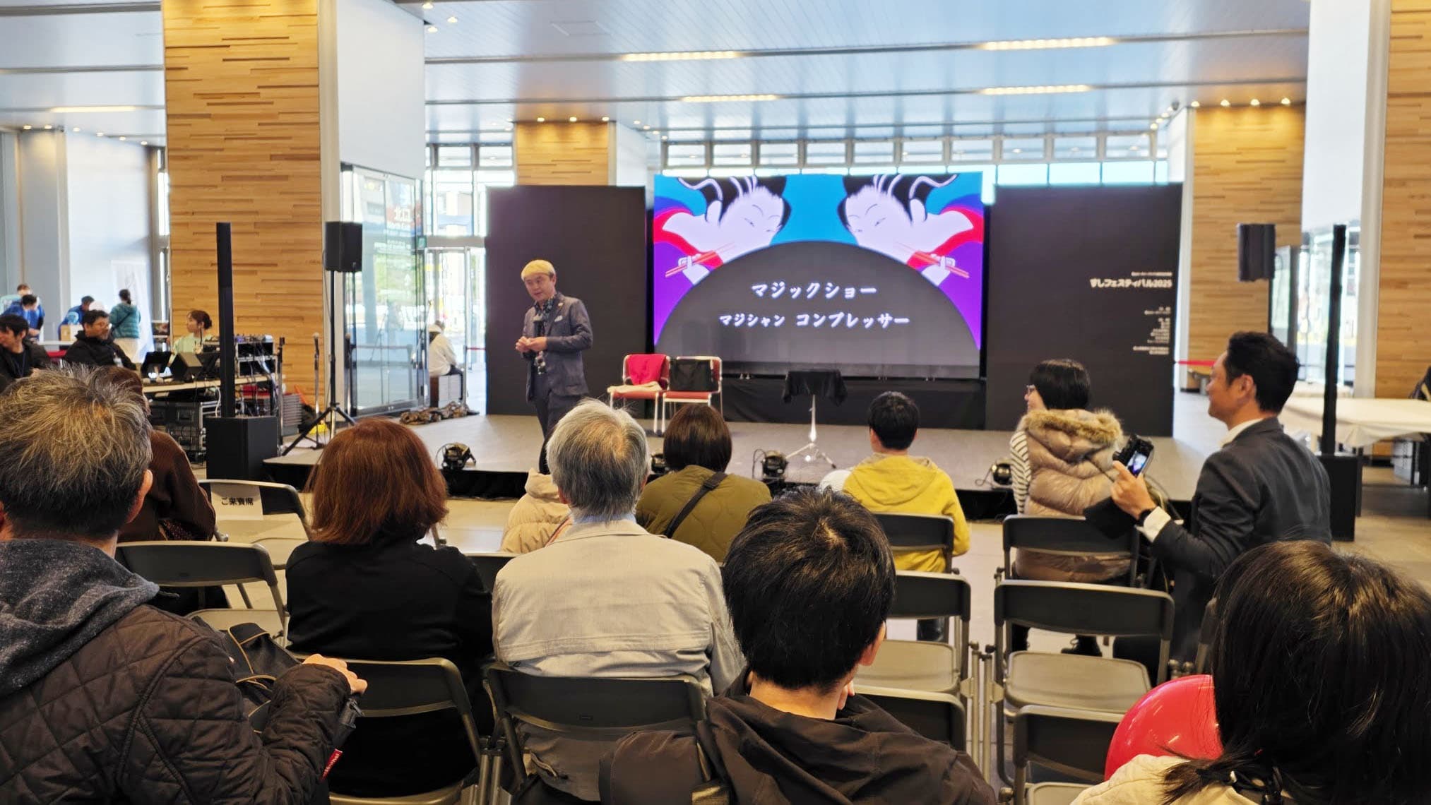 富山駅が巨大な寿司ストリートに!?すしフェスティバル2025出演レポート 7 富山駅南北自由通路で開催されたすしフェスティバル2025のステージで、大勢の観客を前にマジックショーを行うコンプレッサー