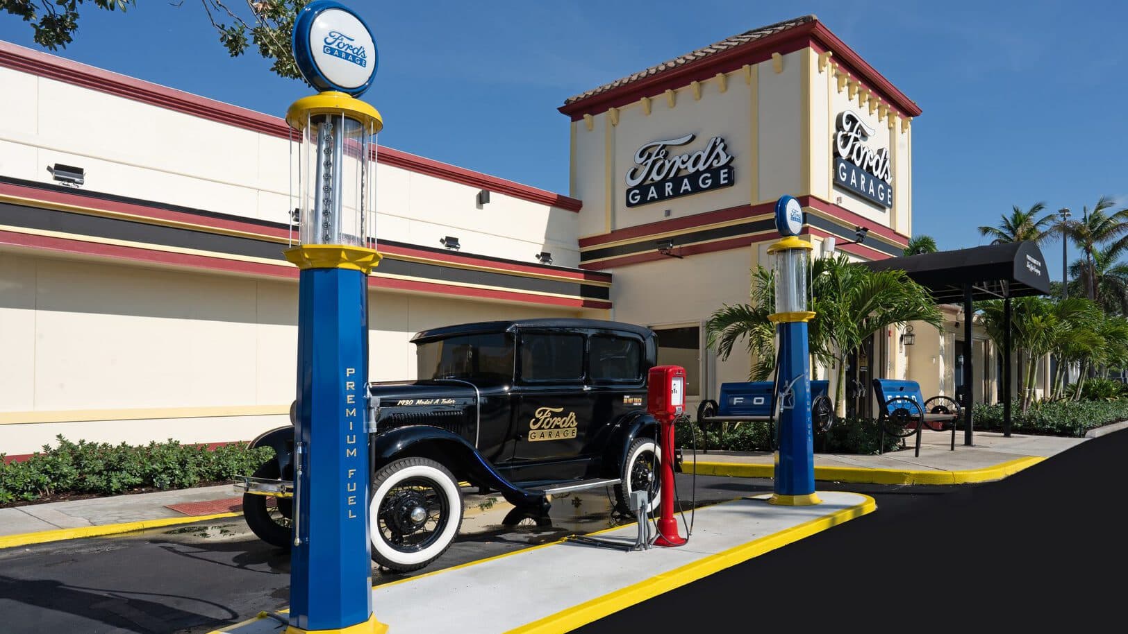 A restored 1930's Model A sits between vintage gas pumps outside a Ford's Garage location. Image Courtesy of Ford's Garage.