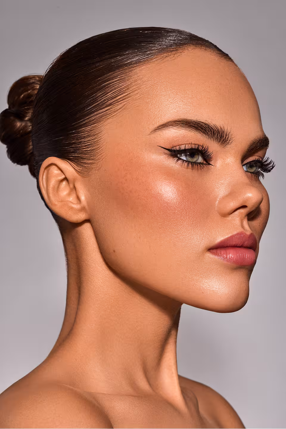 Porträt einer Frau mit elegantem Haarknoten, betontem Make-up und strahlendem Teint.