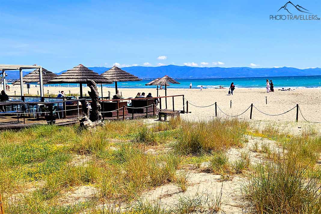 Gäste sitzen unter der Sonnenschirmen einer Beach Bar am Sandstrand Poetto