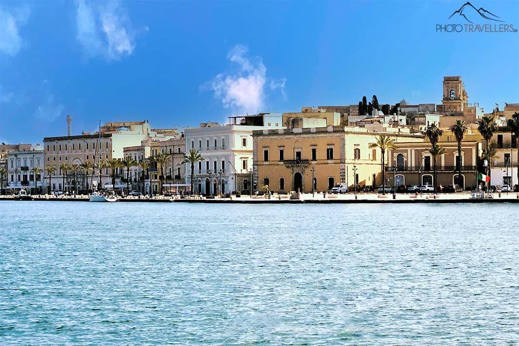 Blick vom Wasser auf die Promenade von Brindisi mit Palmen und hellen Häusern