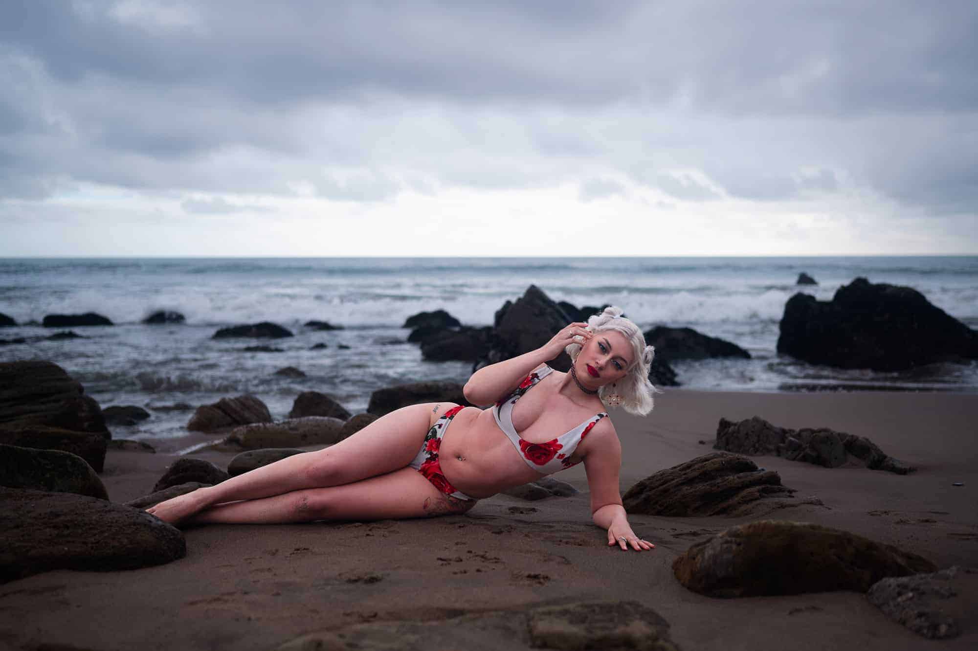 beach boudoir photography of a beautiful woman in a red and white rose bikini lying down on the beach posing on the beach in Los Angeles