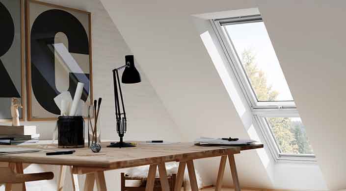 Holztisch unter Dachfenster, einige Bücher und eine Lampe darauf, minimalistischer Raum mit schräger weißer Wand.
