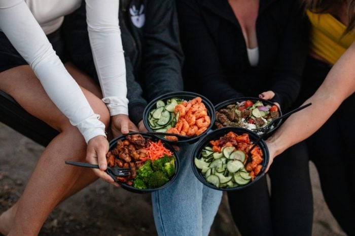 Group of people holding four different Konala protein bowls together showing menu variety