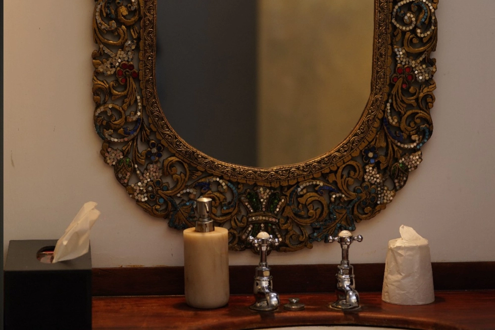 A decorative mirror hangs on the wall in the Connelian room of Adigar's manor, reflecting the elegant surroundings.