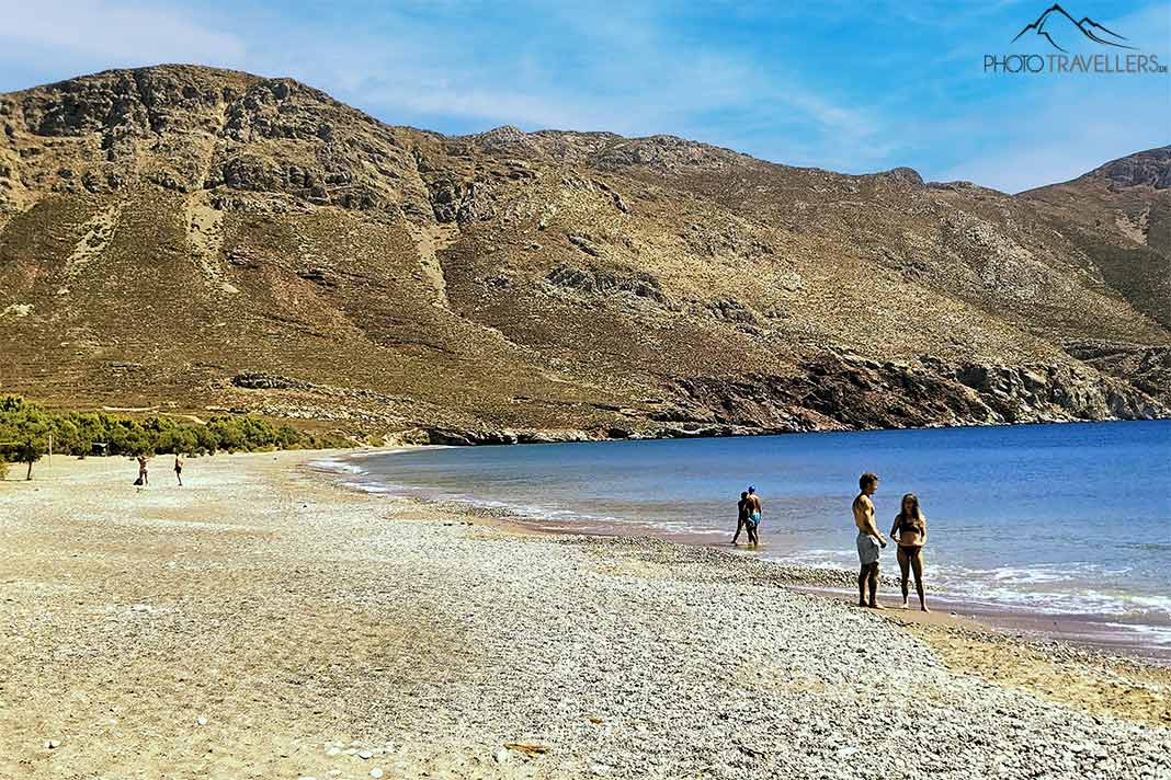 Einzelne Menschen stehen am Strand von Eristos mit Felsen im Hintergrund