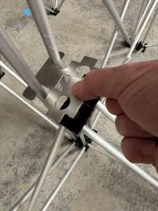 Riser-Leg-Dual-Link-Plate5 - NexGen Portable Staging & Dancefloors Close-up of a hand aligning a perforated metal connector with a scaffolding frame for assembly