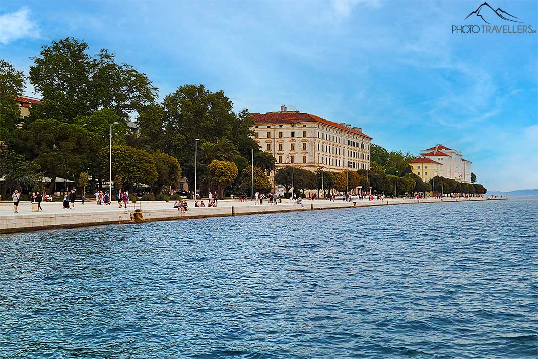 Fußgänger spazieren entlang der Promenade Riva mit Bäumen und Häusern im Hintergrund