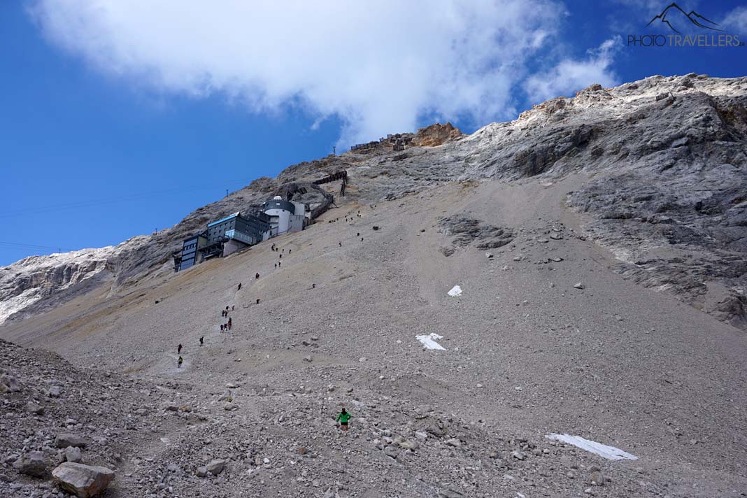 Wanderer steigen neben dem Schneefernerhaus auf dem steilen Geröllfeld in Richtung Zugspitze auf