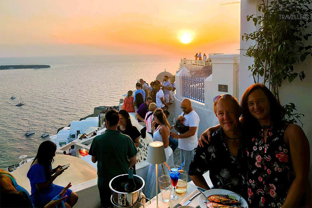 Gäste sitzen zum Sonnenuntergang am gedeckten Tisch einer Taverne in Oia
