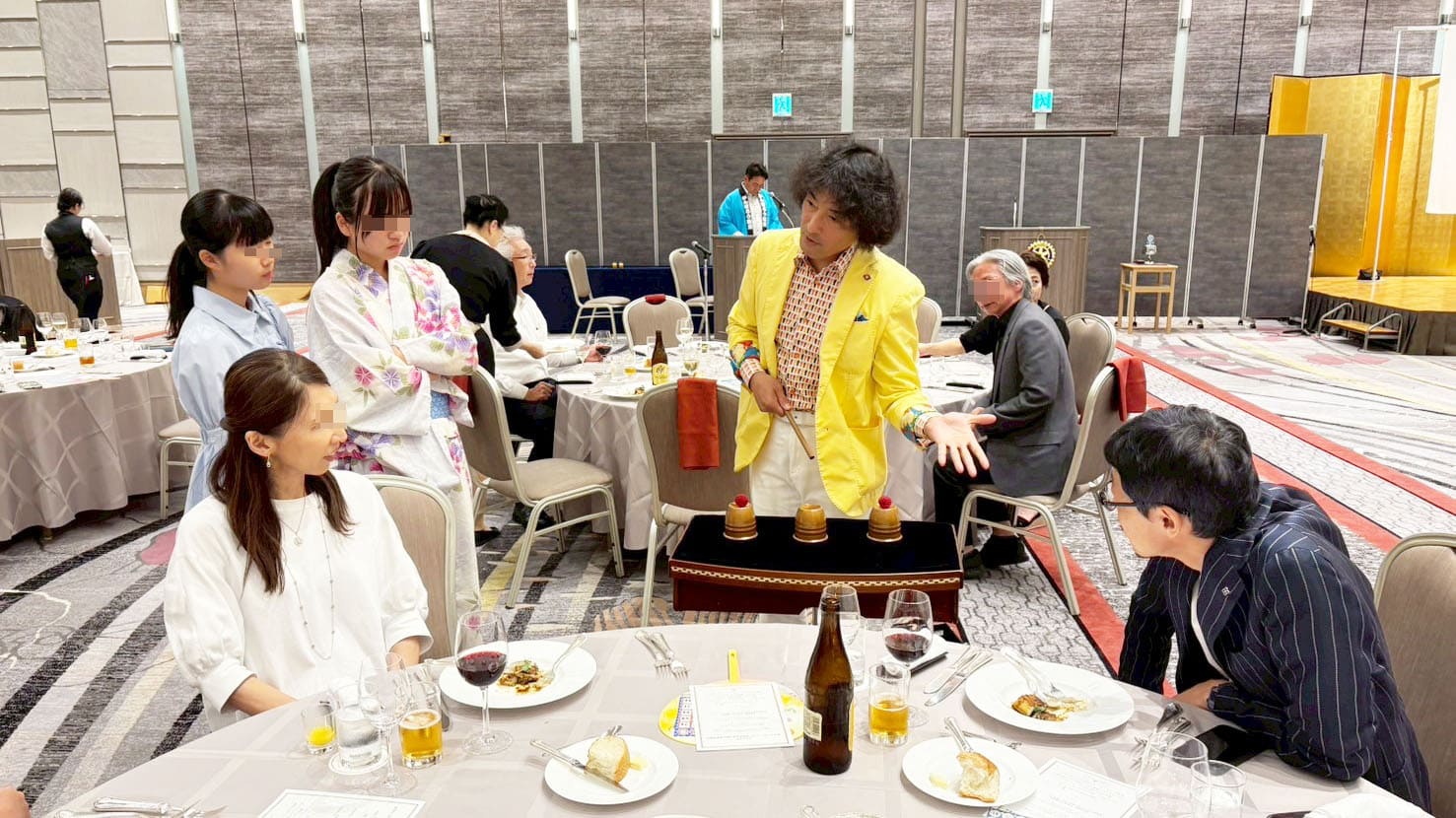 金沢ロータリークラブ パーティーでのマジックショー|石川・富山の笑顔を広げる活動報告 4 ホテル日航金沢での金沢ロータリークラブのパーティーにて、アシスタントのともやんがテーブルマジックを披露し、観客が囲んで楽しんでいる様子。