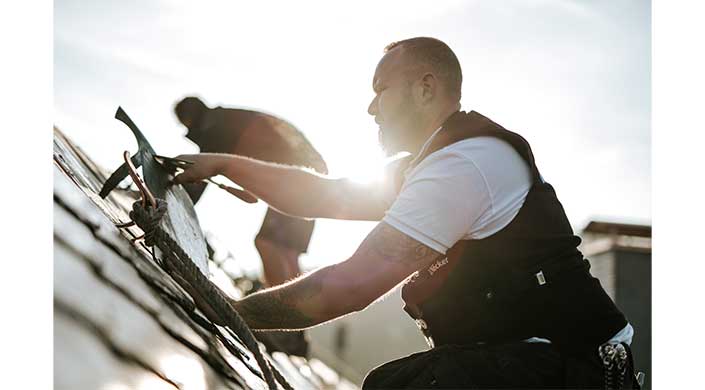 Zwei Männer arbeiten im Sonnenlicht zusammen im Freien, einer trägt ein weißes T-Shirt.