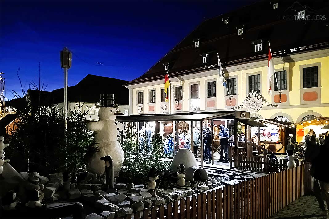 Menschen stehen an der Weihnachtsbahn vor dem beleuchteten Rathaus in Lichtenfels
