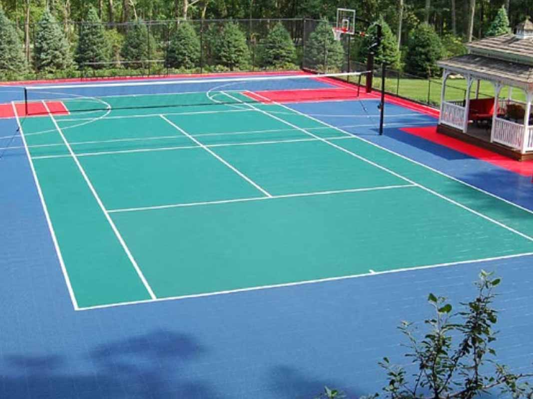 A multi-sport court with markings for basketball, tennis, and volleyball, surrounded by trees and a gazebo on the right side offers the perfect setup for your backyard installation in Huntington.