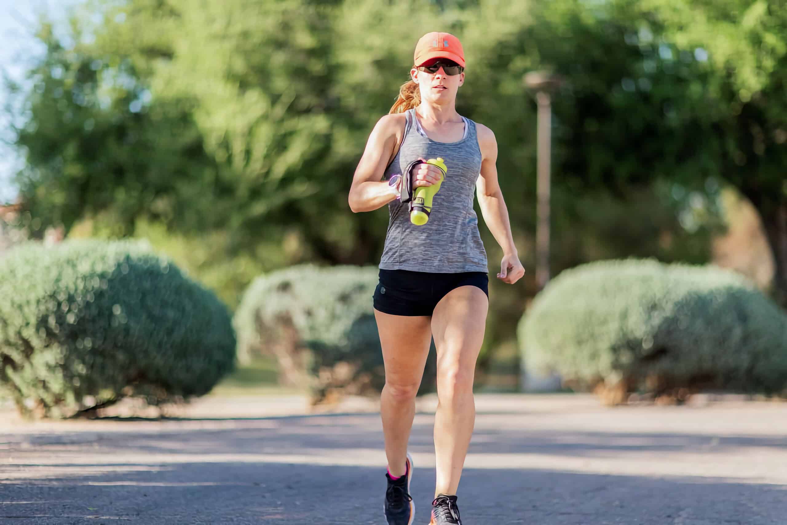 Woman jogging outdoors with water bottle.