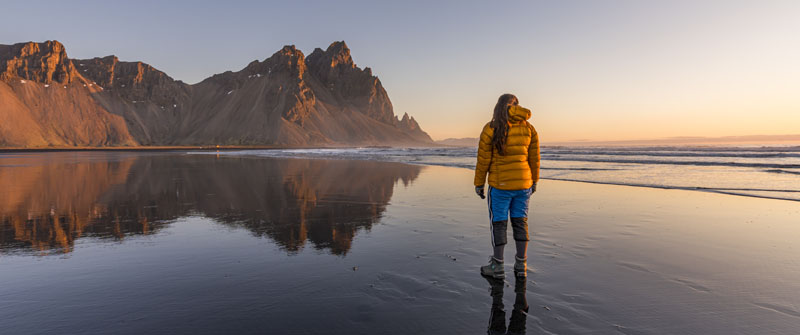 Eine Frau steht am schwarzen Sandstrand von Vik in Island – eine der bekanntesten Sehenswürdigkeiten Islands.