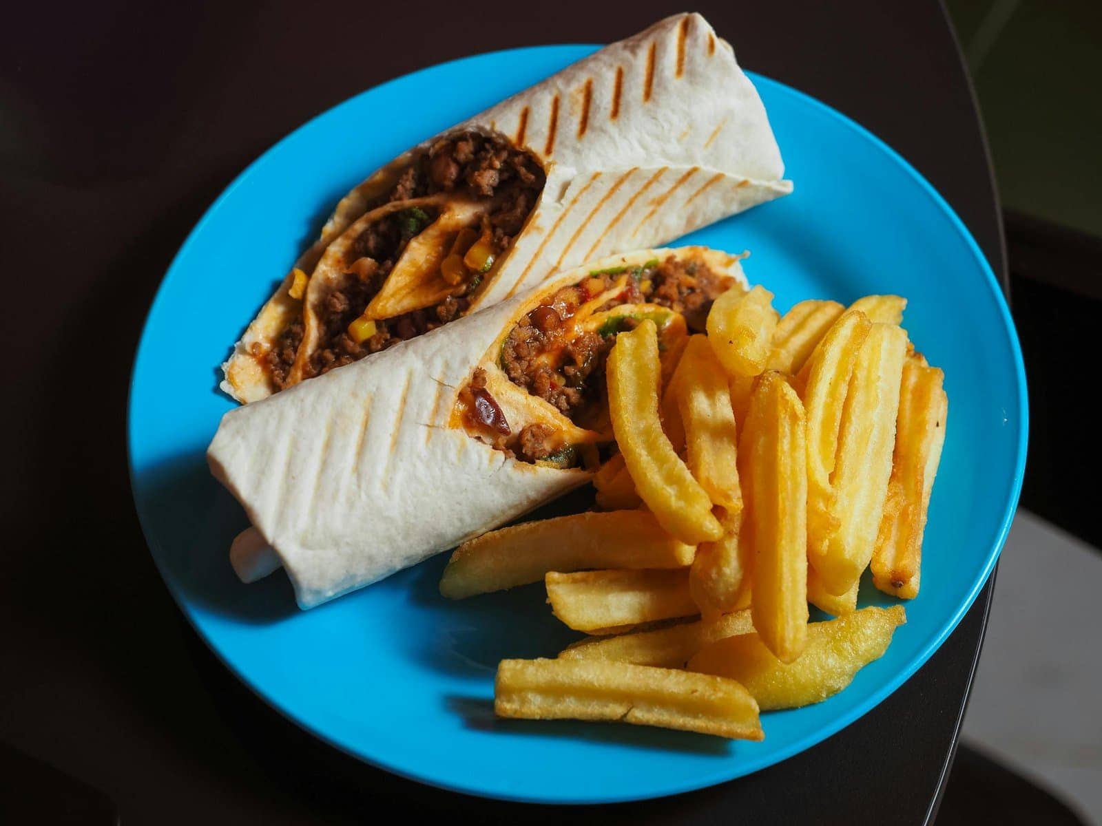 Satisfying burrito wrap with delicious filling, served with crispy french fries on a blue plate.
