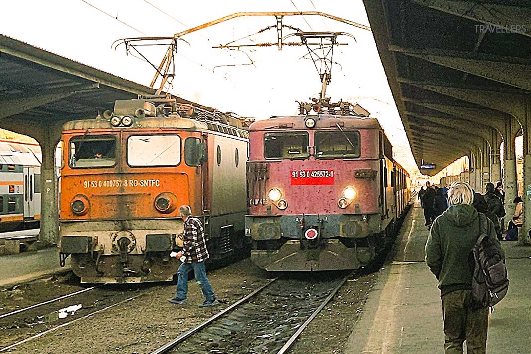 Ein Mann kreuzt die Bahngleise vor zwei sehr alte Lokomotiven
