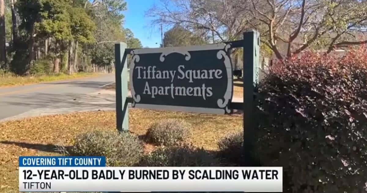 Sign for Tiffany Square Apartments in Tifton, Georgia, where a 12-year-old boy was badly burned by scalding water during a sleepover incident. The sign is set against a backdrop of trees and a blue sky.